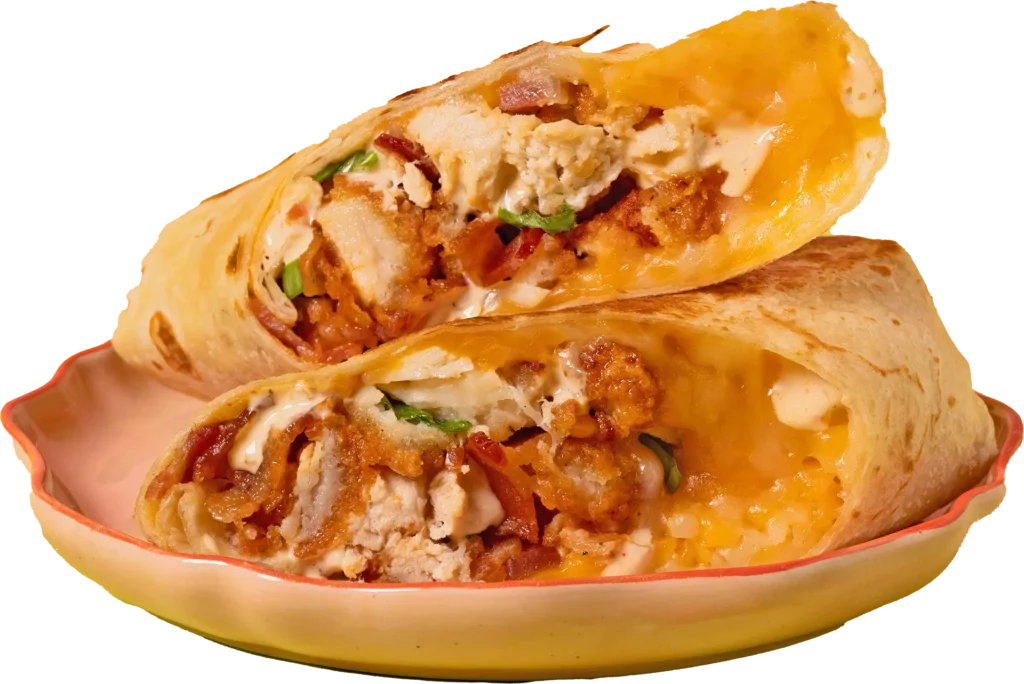 Two halves of a toasted breakfast burrito stacked on a peach-colored plate, filled with crispy chicken, scrambled eggs, melted cheese, and bacon bits.